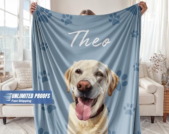May include: A light blue blanket featuring a portrait of a yellow Labrador Retriever with its tongue out. The name "Theo" is written in white script above the dog. Blue paw prints are scattered across the blanket.