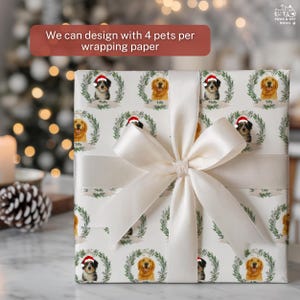 Op de afbeelding: Ingepakte cadeau met gepersonaliseerd cadeaupapier met hondenportretten in kransen, met de tekst "We can design with 4 pets per wrapping paper." Het cadeau is gebonden met een cr&egrave;mekleurig satijnen lint en strik.