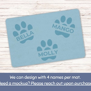 May include: A light blue rectangular pet mat featuring three paw prints with the names "BELLA", "MANGO", and "MOLLY" printed inside. The text "We can design with 4 names per mat" is at the bottom.