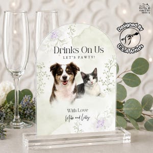 May include: Clear acrylic sign with the text "Drinks On Us" and "Let's Pawty!" featuring a dog and cat illustration. The sign is designed by U.S.A. Artists and includes the names "Mike and Lilly".
