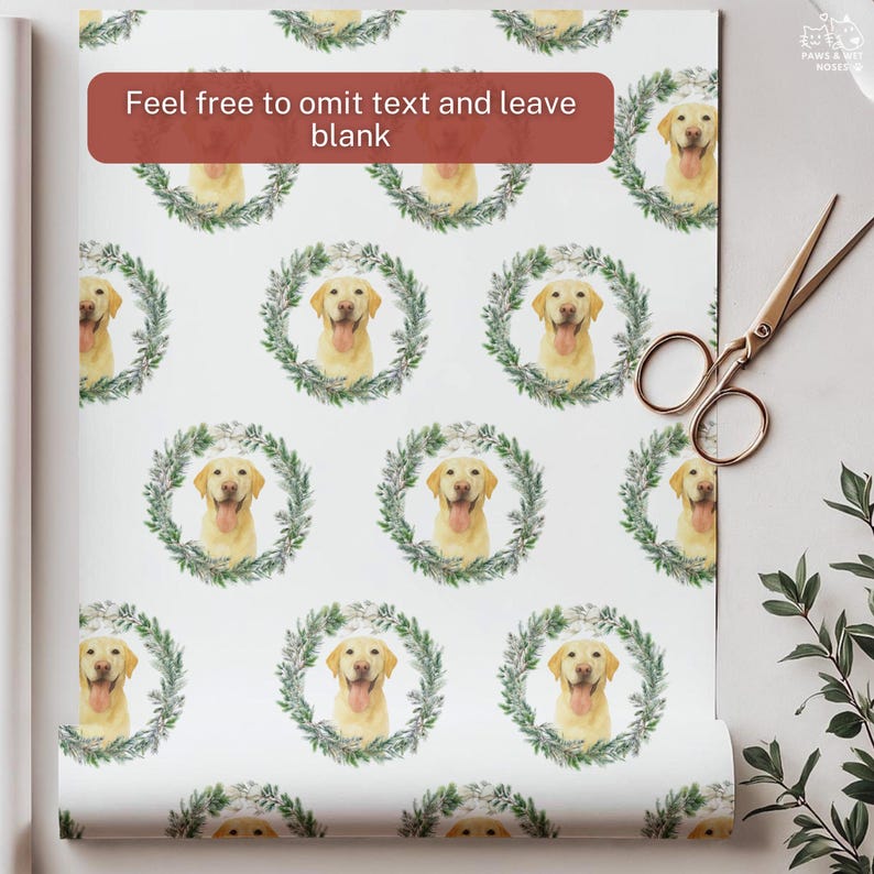 Op de afbeelding: Wit cadeaupapier met een herhaald patroon van gele Labrador Retrievers in groene bladkransen. Een gouden schaar ligt rechts, met een klein takje groen. Het papier is opgerold.
