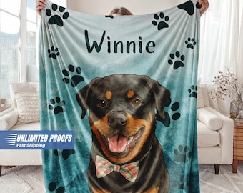 May include: A personalized blanket featuring a Rottweiler dog illustration with a bow tie, the name "Winnie", and paw prints on a teal background. The blanket is held up by a person.