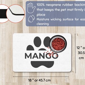 May include: A white pet mat with a black paw print design and the name "MANGO" in bold letters. A stainless steel bowl filled with pet food sits on the mat. The mat is 18 inches long and 12 inches wide.