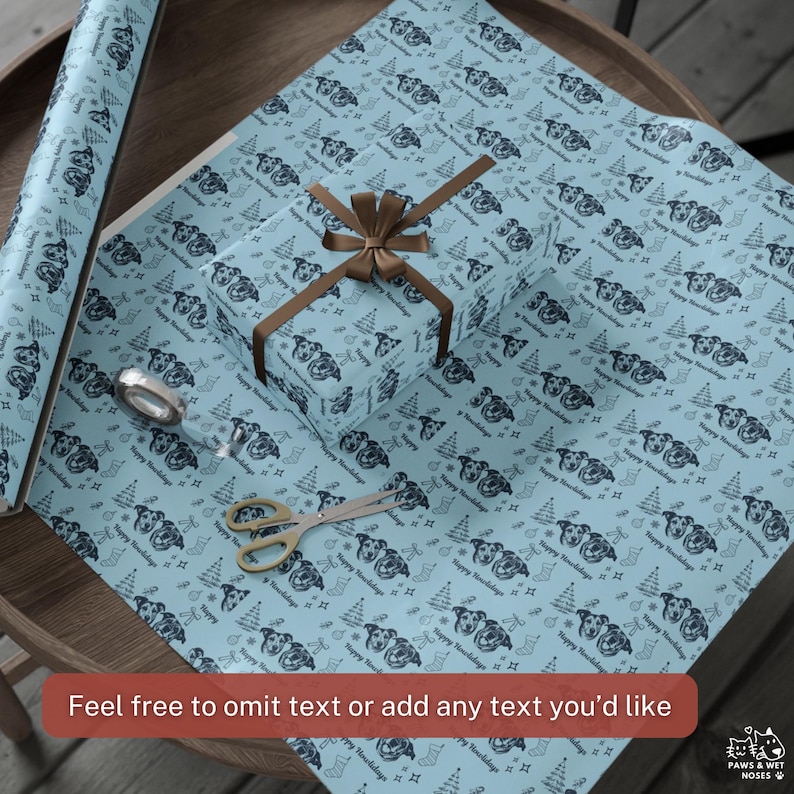 May include: Light blue wrapping paper featuring a repeating pattern of dog faces, Christmas trees, and stockings with the text Happy Holidays. A rectangular gift box is wrapped in the paper with a brown ribbon and a pair of metal scissors.