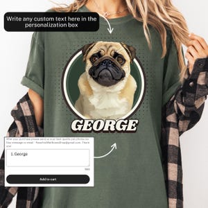 以下が含まれることがあります： オリーブグリーンのTシャツ。グリーンの円の中にパグの肖像画、下に「GEORGE」の文字。パーソナライズされたテキストボックスと「カートに入れる」ボタンが付いています。