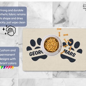 May include: A beige pet food mat with black paw prints and the names "George" and "Mars". A stainless steel bowl filled with kibble sits in the center, surrounded by bone-shaped treats. The mat has text that says "Strong and durable synthetic fabric retains its shape and dries quickly, just wipe clean."