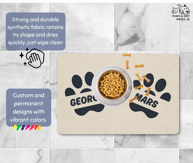 May include: A beige pet food mat with black paw prints and the names "George" and "Mars". A stainless steel bowl filled with kibble sits in the center, surrounded by bone-shaped treats. The mat has text that says "Strong and durable synthetic fabric retains its shape and dries quickly, just wipe clean."