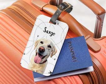 May include: A personalized luggage tag featuring a smiling yellow Labrador Retriever with the name "Sarge" printed above the image. The tag is white with a black leather strap, and is resting on a suitcase with a passport.
