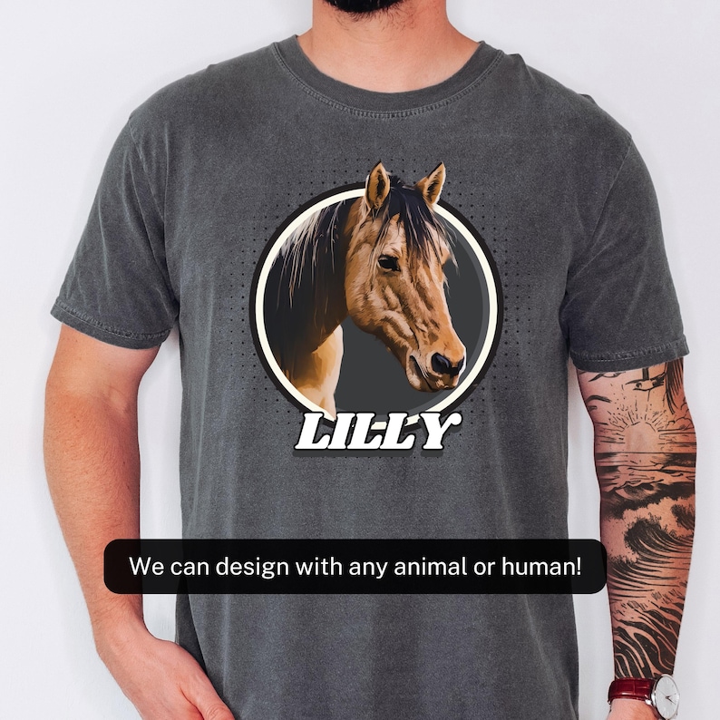 以下が含まれることがあります： 白い円の中に馬の頭のデザインが施された濃い灰色のTシャツ。下には「LILLY」という名前があります。このTシャツには「We can design with any animal or human!」というテキストも含まれています。