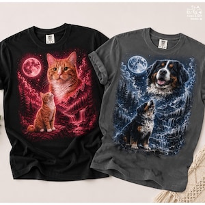 May include: Two graphic t-shirts. One black shirt features a red-toned illustration of a cat with a full moon. The other is a grey shirt with a blue-toned illustration of a dog with a full moon. Both shirts have a crew neck.