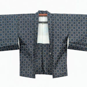 Op de afbeelding: Een donkerblauwe kimono met een herhalend geometrisch patroon van kleine vierkantjes met cirkelvormige centra. Het kledingstuk heeft wijde mouwen, een gestructureerde kraag en een witte binnenvoering zichtbaar bij de opening.