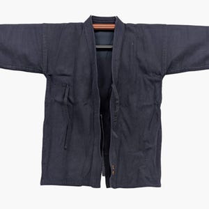 Peut inclure: Une veste de kendo bleu marine foncé présentant un tissage texturé de style sashiko, des manches larges et une ouverture frontale avec des liens en tissu. Le vêtement est fabriqué en coton épais et présente un col structuré et des coutures renforcées.