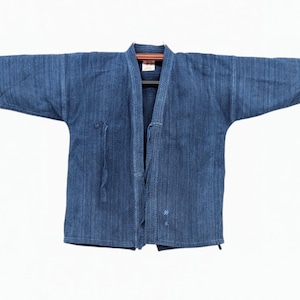 May include: A dark blue indigo-dyed sashiko-stitched jacket featuring a textured quilted pattern, wide sleeves, and a front opening with a small label at the inner collar. The fabric displays a deep blue hue with subtle vertical stitching lines.
