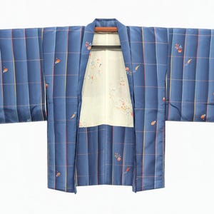 Peut inclure: Une veste kimono bleue ornée d'un motif à carreaux composé de fines lignes rouges et jaunes. Le tissu extérieur présente de petits motifs floraux dispersés en orange et blanc. La doublure intérieure est de couleur crème avec un motif floral discret.