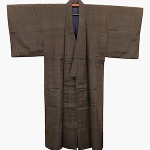 Peut inclure: Un kimono marron foncé présentant un subtil motif à rayures verticales sur tout le tissu. Le vêtement possède des manches larges et rectangulaires ainsi qu'une doublure intérieure bleu marine visible au niveau du col, suspendu sur un cintre.