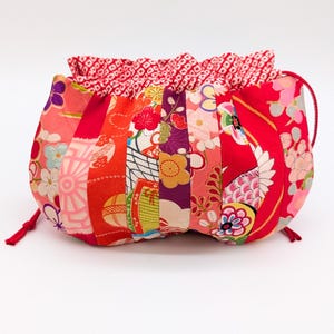 Può includere: Una pochette con coulisse caratterizzata da pannelli verticali di tessuto nelle tonalità del rosso, rosa, arancione e viola. L'esterno presenta vari motivi floreali e geometrici, mentre la fodera interna ha una stampa geometrica rossa e bianca.