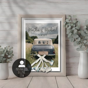 Charming wedding gift showcased in a wooden frame – a poster featuring wedding cars adorned with banknote-made cans. Two white vases on either side of the frame hold eucalyptus arrangements, adding an elegant touch to this unique piece.