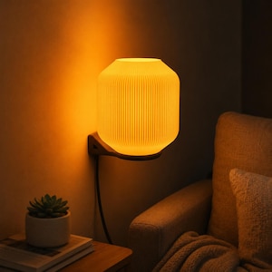 May include: A wall-mounted lamp featuring a cylindrical, vertically ribbed shade that emits a warm, golden-orange glow. The light fixture is attached to a dark, angular bracket and includes a black power cord extending downward from the base.