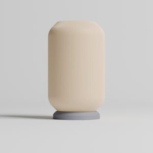 May include: A cream-colored ceramic vase with vertical ridges and a light gray base. The vase is sitting on a white surface.
