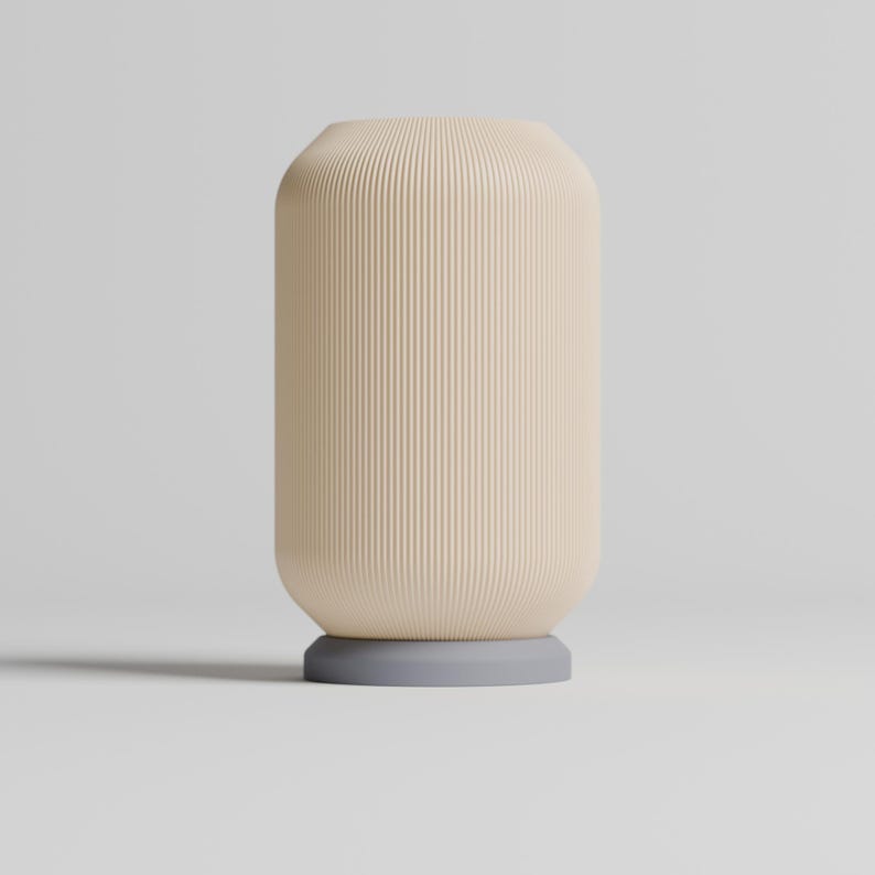 May include: A cream-colored ceramic vase with vertical ridges and a light gray base. The vase is sitting on a white surface.