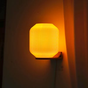 Könnte beinhalten: Eine Wandleuchte mit einem gerippten, orangefarbenen Schirm. Die Lampe ist eingeschaltet und strahlt ein warmes Licht aus.