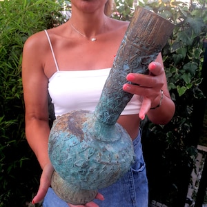 May include: A large, intricately carved, green and brown ceramic vase with a wide base and a tall, slender neck.