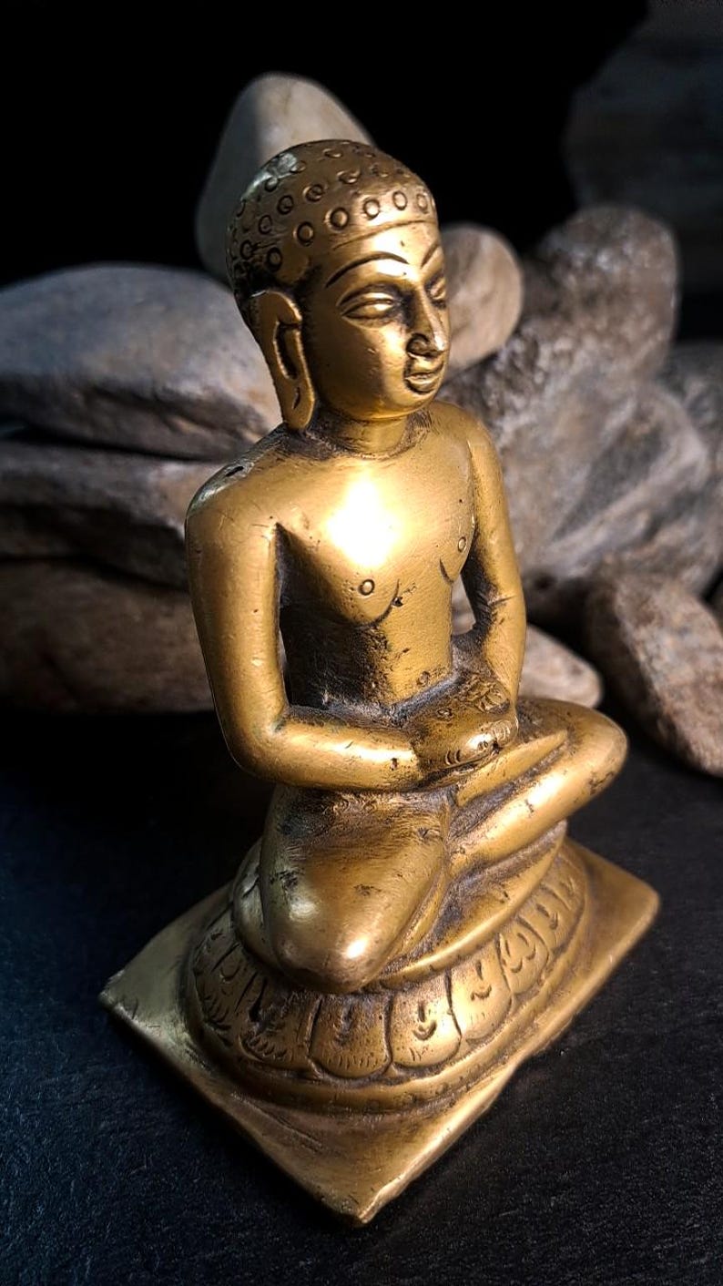 May include: A small, brass statue of a seated Buddha. The statue is highly detailed, with intricate carvings on the base and clothing. The Buddha's face is serene and peaceful, and the overall color is a rich, golden brass. The statue is a collectible item, perfect for meditation or display.