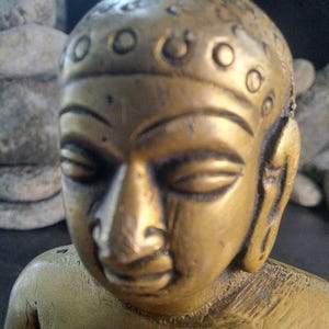 May include: Close-up of a golden brass Buddha statue. The statue has a serene expression and detailed features, including a headdress adorned with small circular accents. The statue's smooth surface reflects light, enhancing its rich golden hue.  The craftsmanship is evident in the intricate facial details and the overall form. This religious artifact is a testament to traditional sculpting techniques and spiritual symbolism.