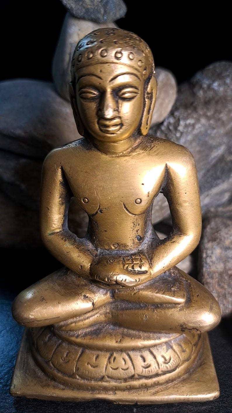 May include: A brass figurine of a seated figure, possibly a deity or spiritual leader, in a meditative pose. The figure has a serene expression and is adorned with intricate details on its head and clothing. The figurine is mounted on a square base with decorative carvings. The overall color is a rich, golden brass.  The statue's smooth surface shows signs of age and wear, adding to its antique appeal. This brass sculpture is a collectible item, ideal for home decor or spiritual practice.