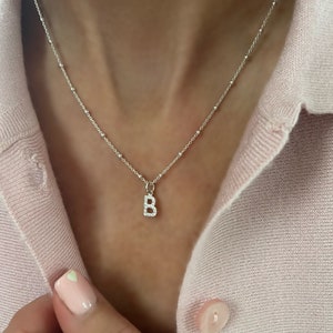 May include: A silver chain necklace with a small letter B pendant. The pendant is made of silver and has small clear stones set into the letter.