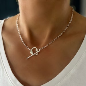 May include: A silver chain necklace with a heart-shaped toggle clasp.