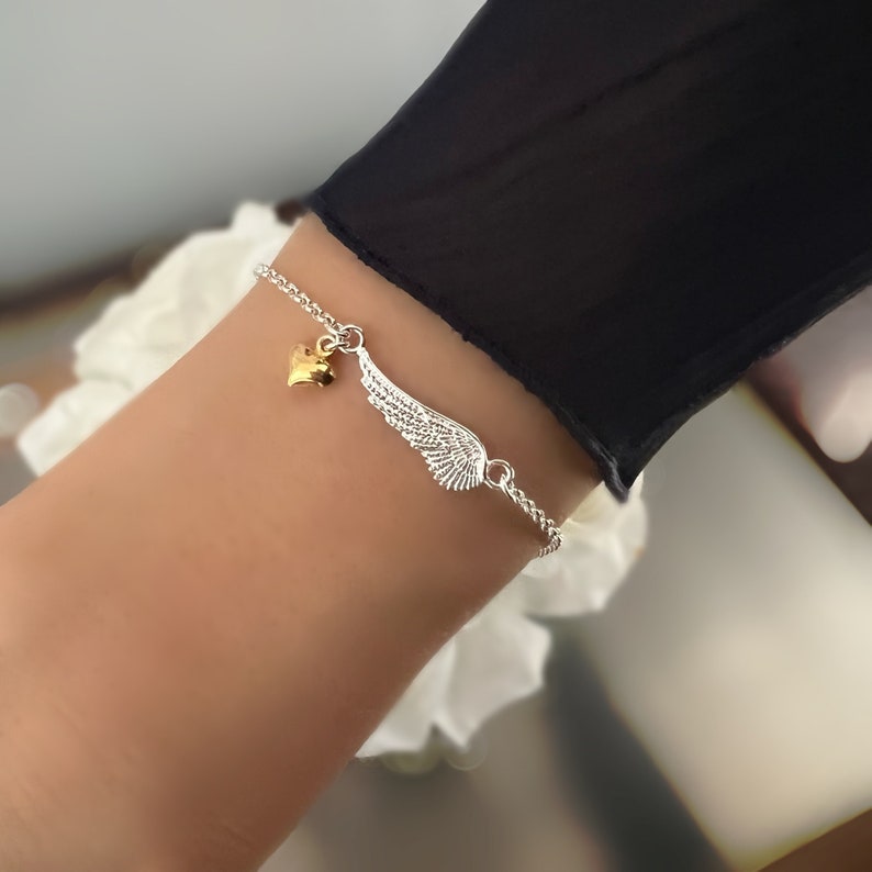 May include: A silver chain bracelet with a gold heart charm and a silver angel wing charm.