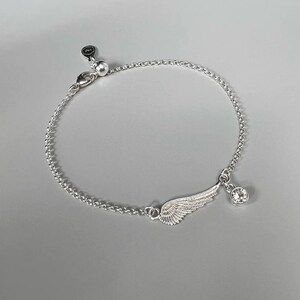 Puede incluir: Un brazalete de cadena de plata con un delicado encanto de ala y un colgante de cristal transparente.