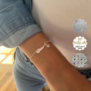 Puede incluir: Pulsera de plata con un ala de &aacute;ngel y un dije de cristal transparente. La pulsera est&aacute; en la mu&ntilde;eca de una mujer. Plata 925. Envoltorio de regalo gratis.