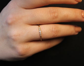 May include: A delicate gold ring with a row of small, clear diamonds set in a simple band.