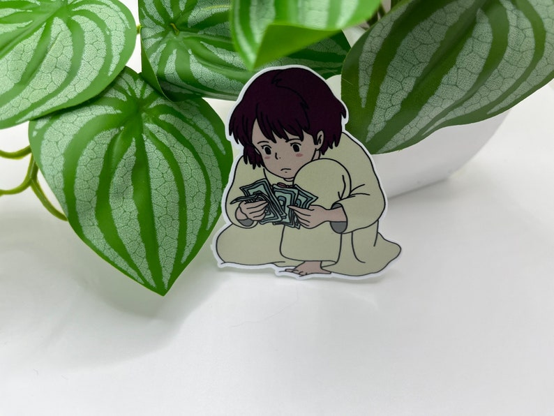 May include: A sticker of a cartoon girl with short brown hair, wearing a light brown robe, sitting on the floor and holding a stack of money in her hands.