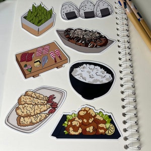 Op de afbeelding: Een set van negen Japanse voedselstickers met verschillende gerechten zoals sushi, edamame, gebakken garnalen, rijst en gefrituurde kip. De stickers zijn gedrukt op wit papier met een glanzende afwerking.