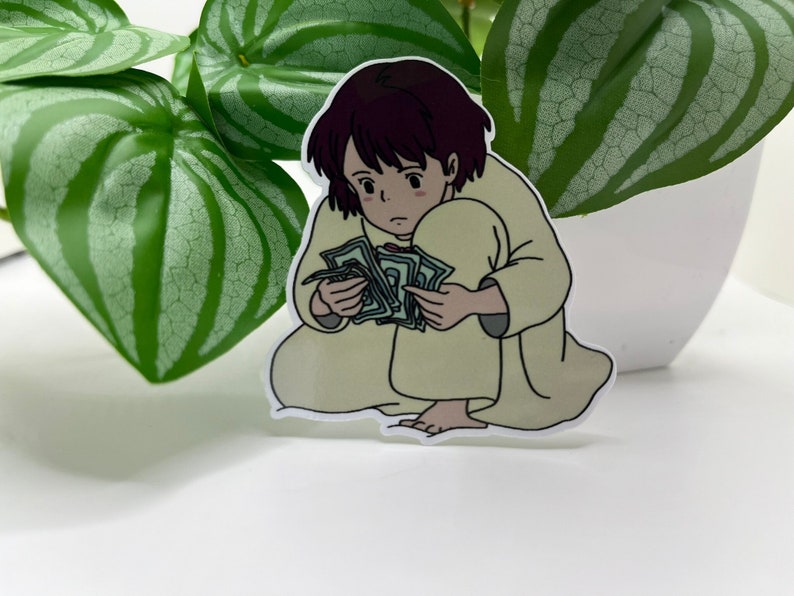 May include: A cartoon sticker of a young person with brown hair, wearing a light yellow robe, sitting and holding a stack of green bills.