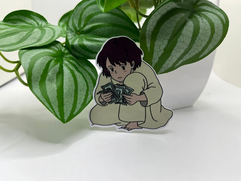 May include: A sticker of a cartoon girl with brown hair, wearing a beige robe, sitting on the floor and holding a stack of money.