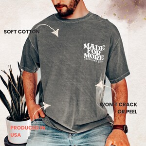 May include: A gray t-shirt with the text "MADE FOR MORE" and "EPHESIANS 2:10" printed on the back. The shirt is labeled "SOFT COTTON" and "WON'T CRACK OR PEEL". The shirt is labeled "PRODUCED IN USA".