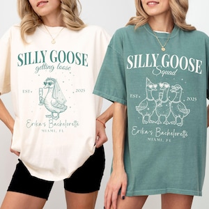 May include: Two oversized t-shirts, one cream and one teal, featuring a "Silly Goose" design. The cream shirt says "getting loose" with a goose in a veil. The teal shirt says "Squad" with three geese wearing party hats and glasses. Both shirts say "Erika's Bachelorette, Miami, FL."