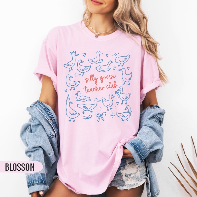 Puede incluir: Camiseta rosa claro con un dise&ntilde;o azul de gansos y el texto "silly goose Teacher club" en rojo y azul. La camiseta es de estilo casual, perfecta para profesores.