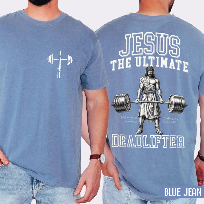 May include: A light blue t-shirt with a white graphic of a barbell and cross on the front. The back of the shirt features the text "JESUS THE ULTIMATE DEADLIFTER" with an illustration of Jesus lifting weights. The words "BLUE JEAN" are at the bottom.