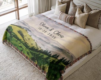 May include: A woven throw blanket featuring a landscape design with green hills, trees, and a mountain range. The blanket has a fringed edge and includes the names "Olivia & Chris" and the date "10-28-2025".