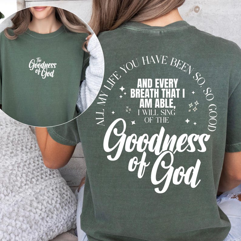 May include: A sage green t-shirt with the text "The Goodness of God" on the front and back. The back of the shirt features the phrase "All my life you have been so, so good" and "Goodness of God".