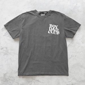 Op de afbeelding: Een donkergrijs t-shirt met de witte tekst "BOY DAD CLUB" op de voorkant. Het shirt heeft korte mouwen en een ronde hals. De stof ziet er zacht en licht vervaagd uit.