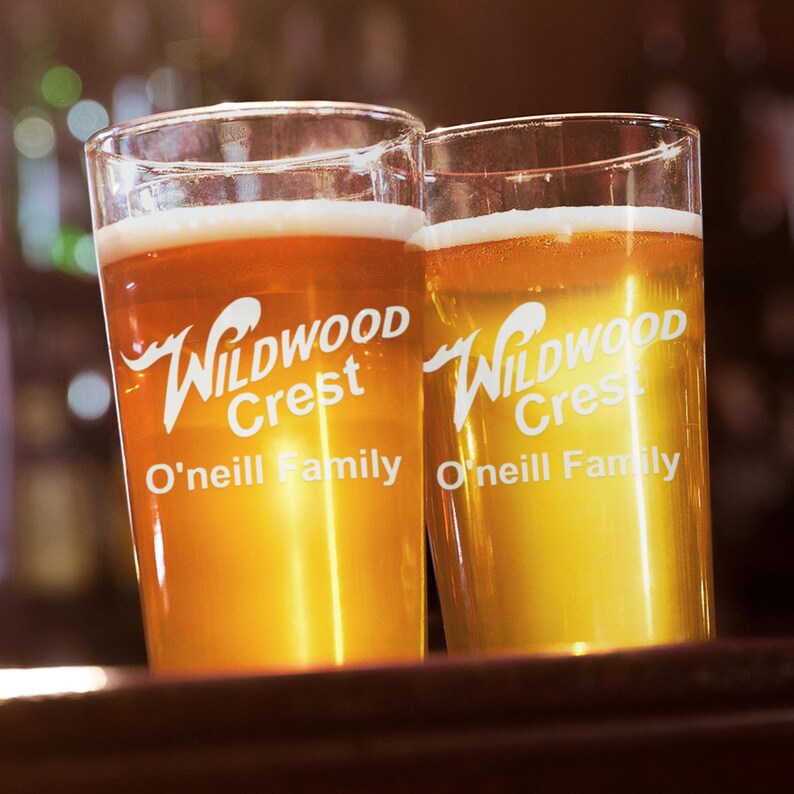 Peut inclure: Deux verres &agrave; bi&egrave;re transparents remplis de bi&egrave;re, avec une t&ecirc;te mousseuse. Les verres portent l'inscription "Wildwood Crest O'Neill Family" en blanc. La bi&egrave;re est de couleur ambre dor&eacute;. L'arri&egrave;re-plan est flou, sugg&eacute;rant un cadre de bar.
