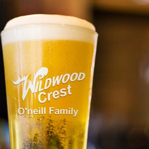 Peut inclure: Un verre de bi&egrave;re blonde avec une &eacute;paisse mousse blanche. Le verre transparent porte l'inscription blanche "Wildwood Crest" et "O'Neill Family". La bi&egrave;re est d'une couleur jaune dor&eacute;.