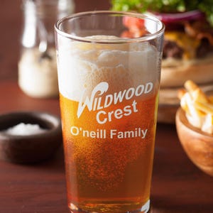 Peut inclure: Un verre transparent rempli de bi&egrave;re et de mousse. Le verre porte les mots "Wildwood Crest" et "O'neill Family". La bi&egrave;re est de couleur ambr&eacute;e.