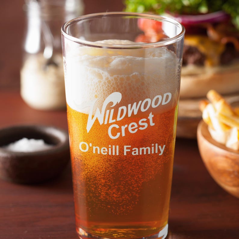 Peut inclure: Un verre transparent rempli de bi&egrave;re et de mousse. Le verre porte les mots "Wildwood Crest" et "O'neill Family". La bi&egrave;re est de couleur ambr&eacute;e.